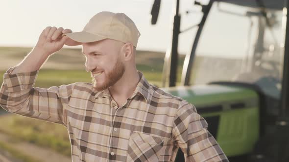 A Young Bearded Farmer is Putting on a Cap and Keeping His Hands on His Belt