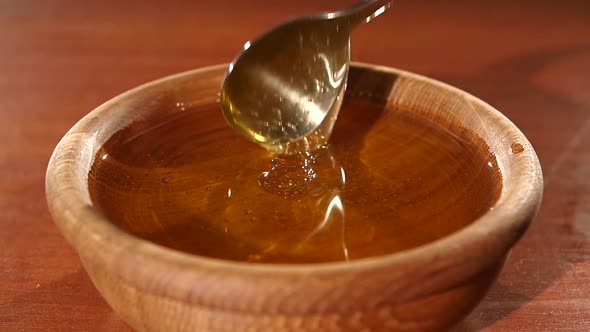 Taking Honey By Metal Spoon in Wooden Bowl, Flowing Down, Slow Motion