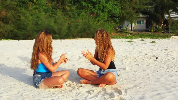 Young happy ladies on photoshoot spending quality time at the beach on sunny blue and white sand 