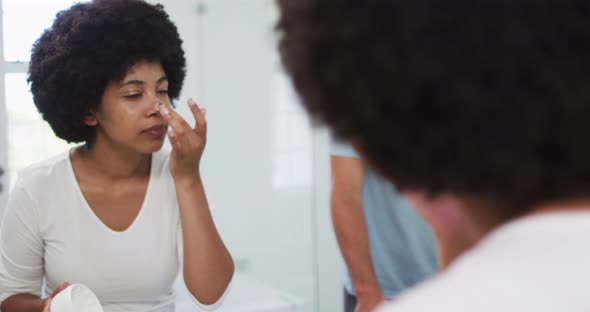 African american woman applying face cream while looking in the mirror at home