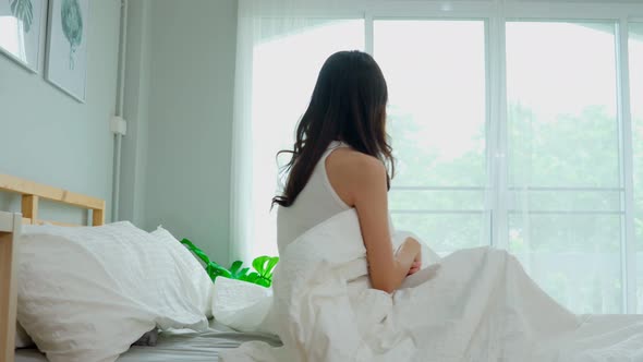 Back of view Woman stretching her arm after wake up on bed and looking outside windows