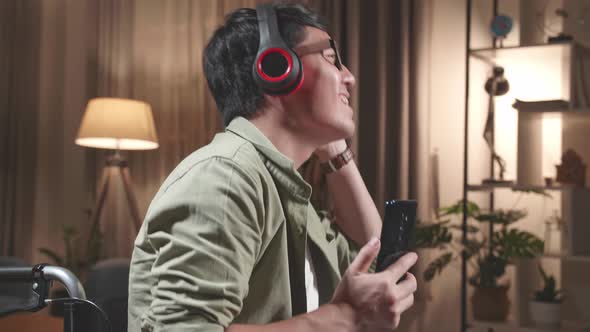 Man Sitting In A Wheelchair Use Mobile Phone And Listening To Music With Headphones And Dancing