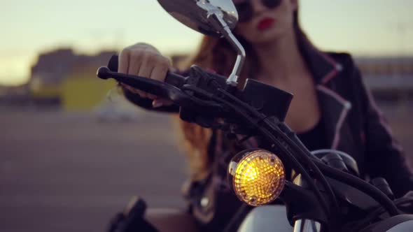 Portrait of a Female Biker in Leather Jacket and Shorts Sitting on Her Bike and Holding a Handlebar