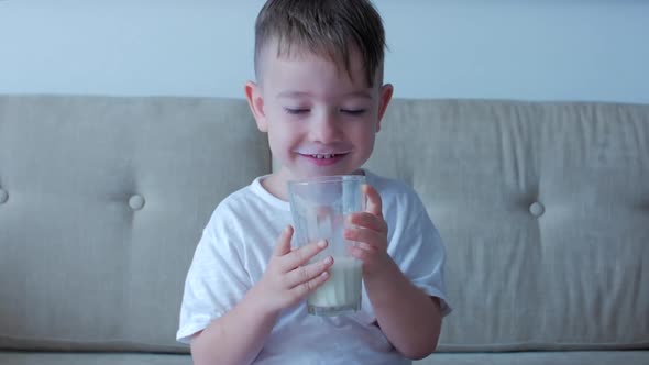 Cute Baby Boy Drinking a Glass of Milk Sitting on the Couch at Home. Slow Motion Little Boy Drinking