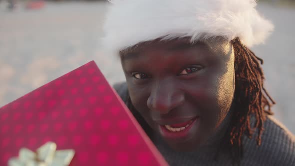 Happy Black Man with Santa Hat Holding Red Wrapped Christmas Gift