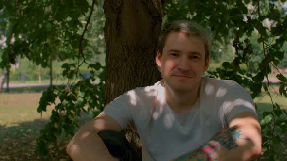 Young Man Rests Sitting Near Tree Trunk in Parkland