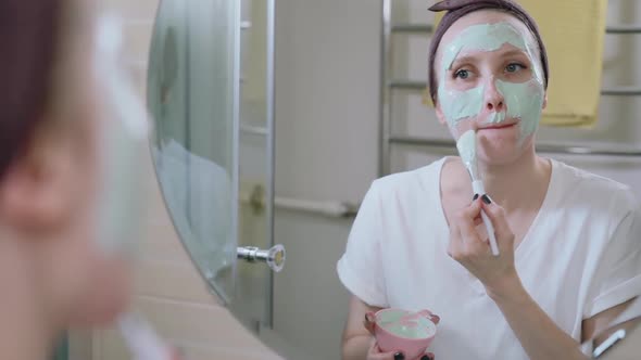 Young Beautiful Woman Smears Cosmetic Mask on Face While Having Time in Home Interior Spbas