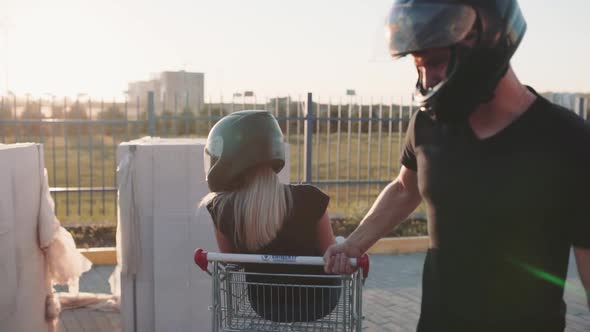 Guy Rolls Attractive Young Woman in the Trolley in Motorcycle Helmets at Sunset