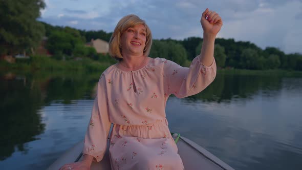 Smiling Caucasian Trans Woman in Pink Dress Admiring Golden Sunset Sitting in Boat on Summer Lake