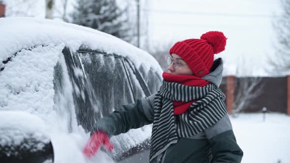 Young woman cleans snow from her car in the yard and sits down to start car