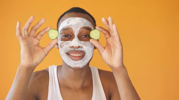 Happy Black Man Poses for the Camera with a Cosmetic White Mask on His Face and a Slice of Cucumber