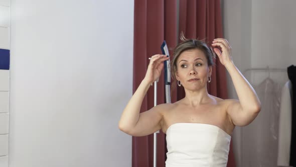 an Attractive Woman with Blonde Hair Corrects the Hairstyle in Front of Mirror