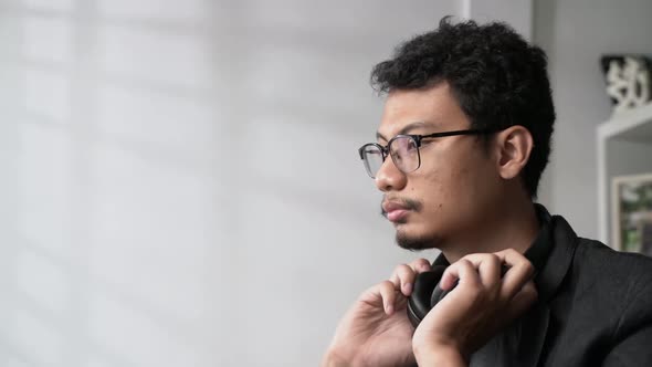 handsome Asian man with glasses hanging headphones around his neck