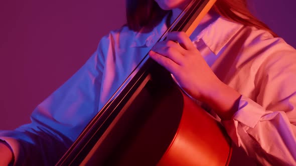 Talented woman playing the cello on neon background, side view, closeup. Studio shooting.