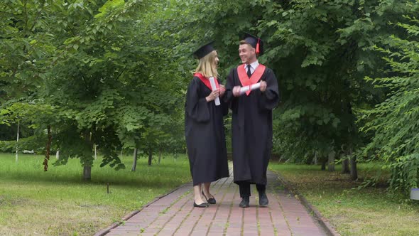 Young Happy Graduates Holding Diplomas and Walking in Park Talking and Relaxing