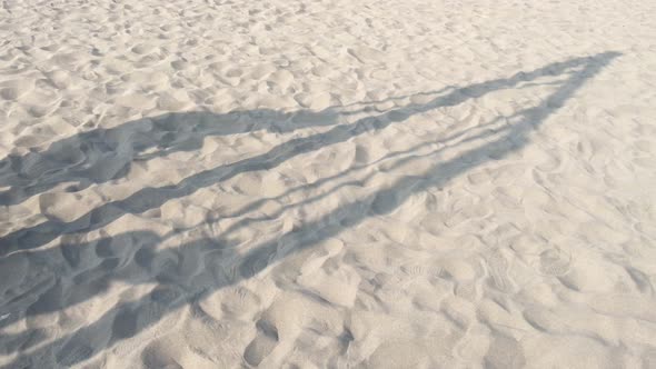 The shadow of a child playing with an rope swing in a desert or sandy beach.