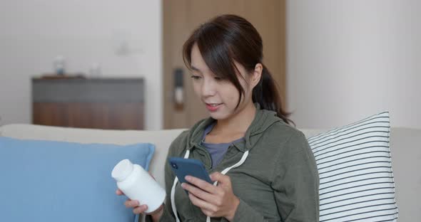 Woman check the ingredients of the bottle of medicine with mobile phone at home