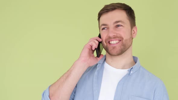 Young Man with Smartphone in Hands He is Talking and Laughing Isolated on Yellow Background