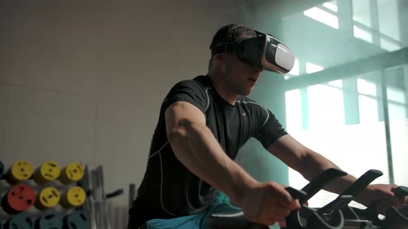 Professional Athlete Performs Sport Exercise on Bicycle Simulator in VR Helmet