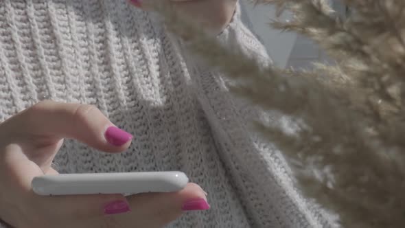 Woman in Cozy Sweater Drinking Cup of Morning Coffee and Using Mobile Phone