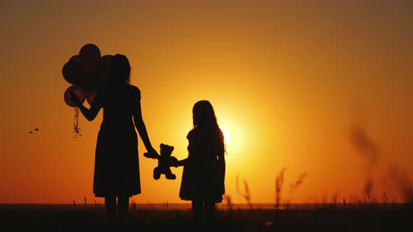 Mom and Daughter Admire the Sunset, Hold Balloons and a Teddy Bear