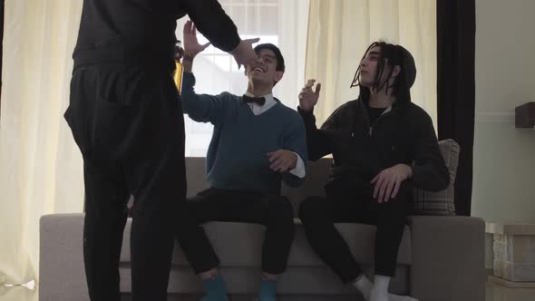 Young Caucasian Men Welcoming Their Friend Bringing Beer. Three Joyful University Students Sitting