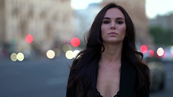 a Brunette with Long Hair and in Black Clothes Walks Against the Background of a Blurred City Street