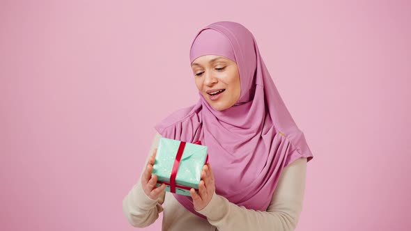 Pleased Middle Aged Islamic Woman Holding Gift Box Shaking It and Smiling to Camera in Appreciation