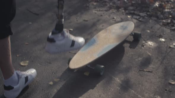 A Young Man with a Metal Bionic Prosthetic Leg is Riding a Skateboard in the Autumn Forest