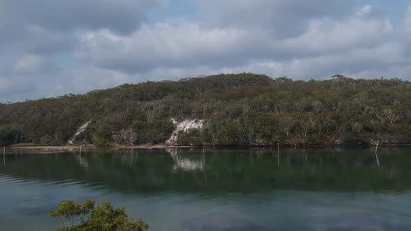 A large Australian billabong surrounded by rugged native bush and steep sandstone cliffs on a cloudy