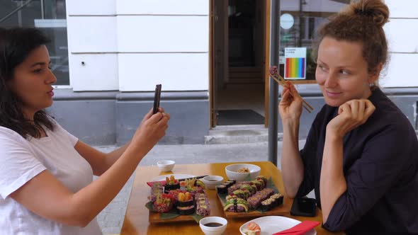 Young Woman Taking Picture of Her Friend Enjoining Sushi During Lunch