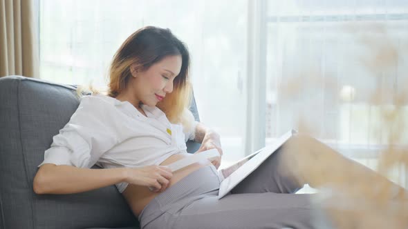 Asian young beautiful pregnant woman applying headphones on her belly.