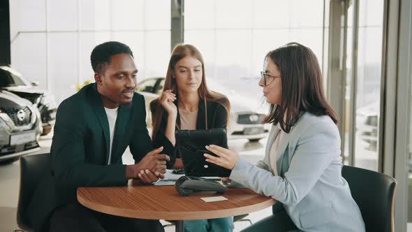 African Man and Caucasian Woman Talking with Female Car Dealer at Auto Salon