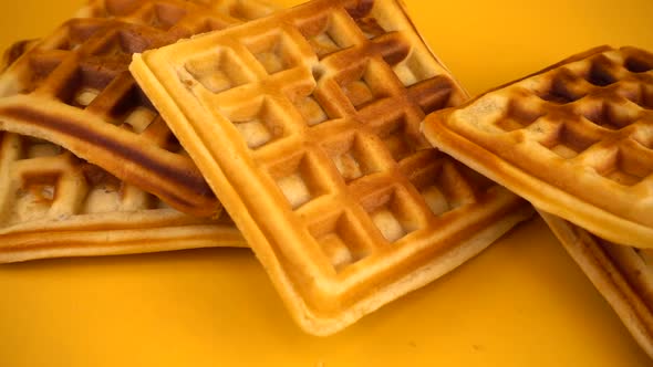 Belgian waffles are falling down on a yellow background. Slow motion.