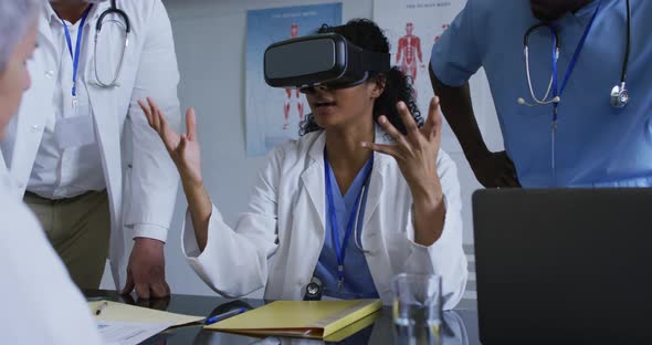 Asian female doctor at table using vr headset with a diverse group of colleagues gathered around her