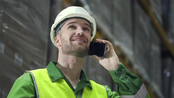 Portrait of American Man Talking on Phone Standing in Warehouse During Working Day.