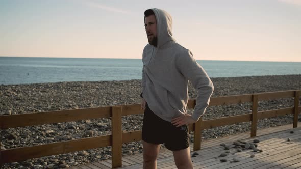 Athletic Man Is Doing Tilts of Torso and Stretching Hands on Sea Coast