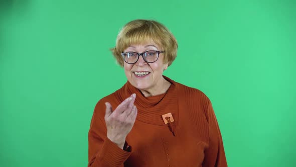 Portrait of Senior Woman Is Waving Hand and Showing Gesture Come Here Isolated Over Green Background