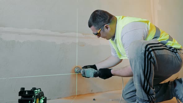 Construction Worker Drills a Hole in the Wall Under the Socket