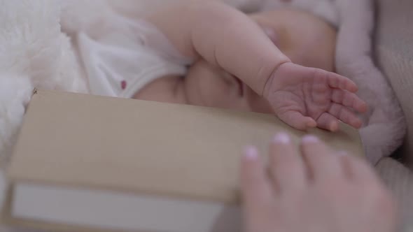 Closeup Sleeping Little Baby Girl in Bed with Female Hand Taking Away Book in Slow Motion