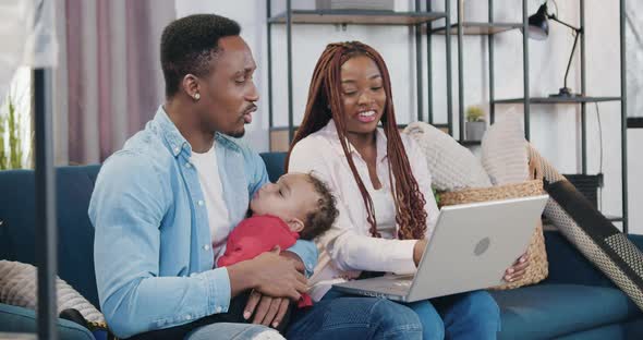 Man Holding His Baby on Hands Sitting with His Wife on Sofa in Contemporary Living-Room