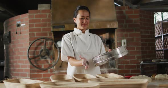 Animation of of happy asian female baker sieving flour on board