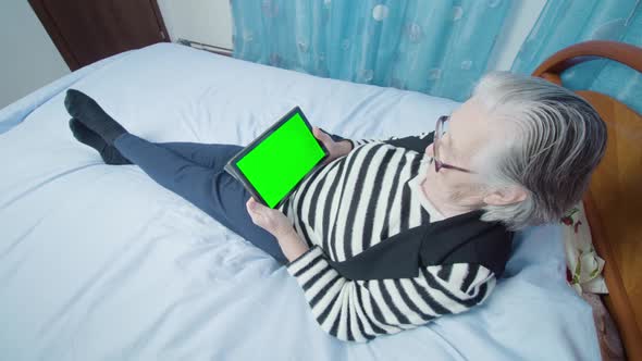 Woman with Grey Hair Reads News Via Tablet Lying on Bed