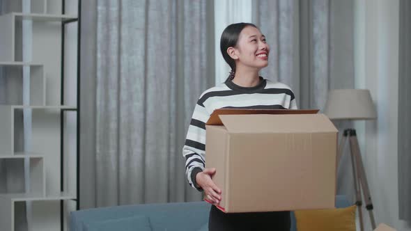 Smiling Young Asian Woman Carrying Cardboard Box With Stuff Into A New House Then Looking Around