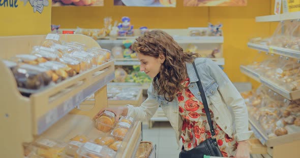 Young Pretty Girl Chooses Flour Products on the Shop Window of the Bakery