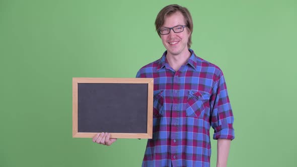 Happy Young Hipster Man Holding and Pointing at Blackboard