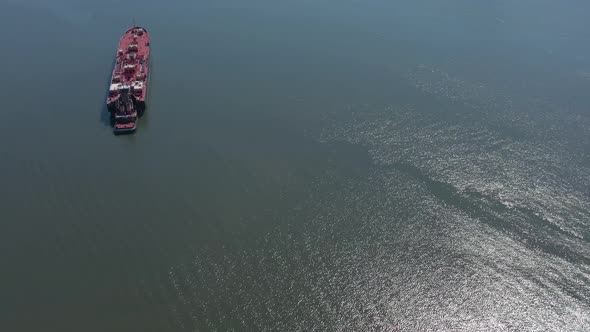 A drone view of a large red barge on the Hudson River in NY on a sunny day. The camera boom down and