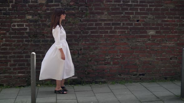 Gimbal Shot of Woman Walking in White Long Dress on Brick Wall Background
