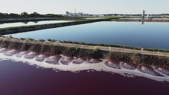 Aerial view of a red-colored wastewater reservoir near an industrial plant.