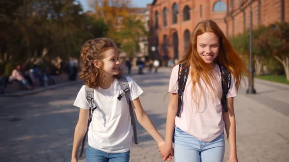 Happy Preteen Schoolgirls Walking Outdoors, Holding Hands and Talking